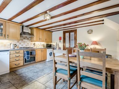 A kitchen with wooden cabinets a dining table with chairs and a vase with flowers at West End Barn in Cleeve Prior near Evesham