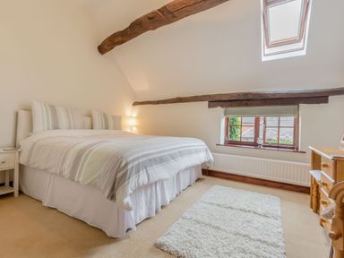 A bedroom with a double bed striped bedding wooden beams on ceiling a window and a wooden dresser at West End Barn in Cleeve Prior near Evesham