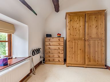 A bedroom corner with wooden dresser and wardrobe next to a window at West End Barn in Cleeve Prior near Evesham