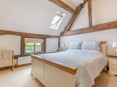 A bedroom with a large bed wooden beams and skylight window at West End Barn in Cleeve Prior near Evesham