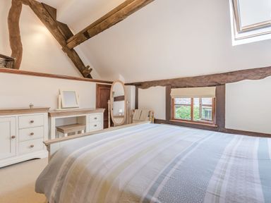 A bedroom with a bed a dresser a mirror and wooden beams at West End Barn in Cleeve Prior near Evesham