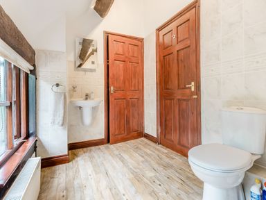 A bathroom with wooden doors a toilet a wall-mounted sink a mirror and a window with a roller blind at West End Barn Cleeve Prior near Evesham