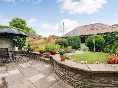 An outdoor patio with a table and chairs under a black umbrella surrounded by a stone wall and plants at West End Barn Cleeve Prior near Evesham