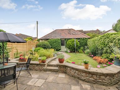 A garden with a lawn surrounded by plants and flowers a paved patio area with table umbrellas and chairs and a small building covered in ivy at West End Barn in Cleeve Prior near Evesham