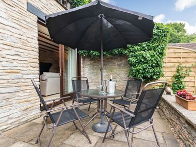 An outdoor patio with a round glass table four black chairs a black umbrella and a stone wall at West End Barn in Cleeve Prior near Evesham