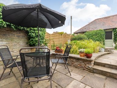 An outdoor patio with a glass table black chairs and an umbrella next to a stone wall with potted plants at West End Barn in Cleeve Prior near Evesham