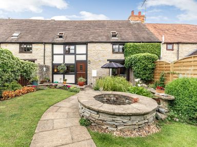 A garden with a stone well lawn plants and flowers in front of a stone house at West End Barn in Cleeve Prior near Evesham