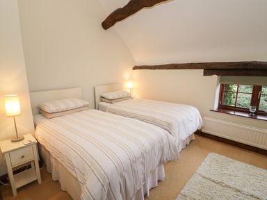 A bedroom with two single beds side by side with striped bedding a bedside table with a lamp rustic wooden beams on the ceiling and a window with a view at West End Barn in Cleeve Prior near Evesham