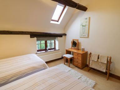 A bedroom with two single beds a wooden dressing table with a mirror and stool a towel rack and a window at West End Barn in Cleeve Prior near Evesham
