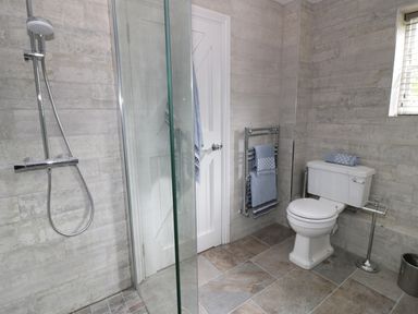 A bathroom with a shower, toilet, towel rack, and a window at Pebworth Cottage in Pebworth near Stratford-upon-Avon