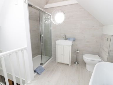 A bathroom with a shower cubicle a sink on a cabinet a toilet and a round window at Pebworth Cottage Pebworth near Stratford-upon-Avon
