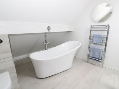 A bathroom with a freestanding bathtub a towel rack with towels and a round mirror at Pebworth Cottage Pebworth near Stratford-upon-Avon