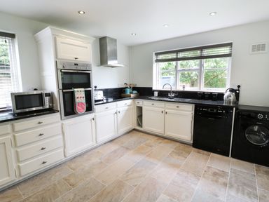 A kitchen with white cabinets black countertops and appliances including microwave oven dishwasher and washing machine at Pebworth Cottage in Pebworth near Stratford-upon-Avon