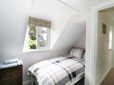 A small bedroom with a single bed and plaid bedding next to a window and dresser at Pebworth Cottage Pebworth near Stratford-upon-Avon