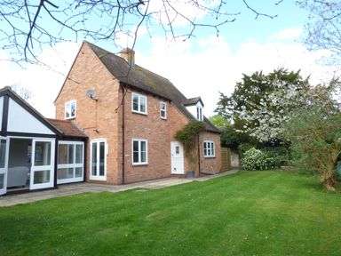 A brick house with a white framed glass extension and garden with grass and trees at Pebworth Cottage in Pebworth near Stratford-upon-Avon