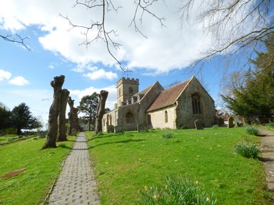 A stone church with a tower and surrounding gravestones along a stone path with pruned trees at Pebworth Cottage Pebworth near Stratford-upon-Avon