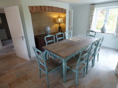 A dining room with a wooden table and blue chairs near a window with curtains at Pebworth Cottage Pebworth near Stratford-upon-Avon