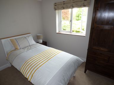 A bedroom with a single bed a bedside table with a lamp a window and a wooden wardrobe at Pebworth Cottage in Pebworth near Stratford-upon-Avon