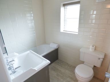 A bathroom with a sink, bathtub with a rolled towel, toilet, and a window at Pebworth Cottage Pebworth near Stratford-upon-Avon