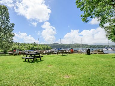 A grassy park with picnic tables near a lake with docks and boats at Claife View Lodge in Troutbeck Bridge