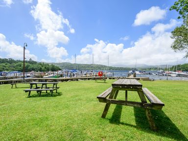A grassy area with wooden picnic tables near a dock with boats on a lake at Claife View Lodge in Troutbeck Bridge