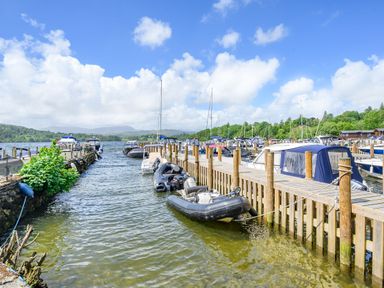 A dock with boats moored on a lake with hills and trees in the background at Claife View Lodge in Troutbeck Bridge
