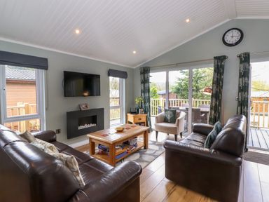 A living room with leather sofas a wooden coffee table sliding glass doors and a wall clock at Claife View Lodge in Troutbeck Bridge