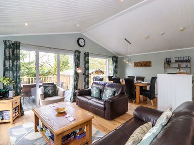 A living room with leather sofas wooden coffee table dining table and chairs sliding glass doors with patterned curtains at Claife View Lodge in Troutbeck Bridge