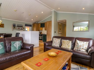 A living room with brown leather sofas wooden coffee table and kitchen area at Claife View Lodge in Troutbeck Bridge