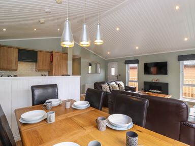 A dining table with plates and mugs next to a living area with sofas a TV and fireplace at Claife View Lodge in Troutbeck Bridge
