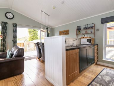 A kitchen area with wooden and black cabinets next to a dining table with chairs and a living room with a brown leather sofa at Claife View Lodge in Troutbeck Bridge