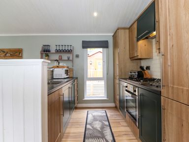 A kitchen with wooden cabinets a gas stove a microwave and a window with a roller blind at Claife View Lodge in Troutbeck Bridge