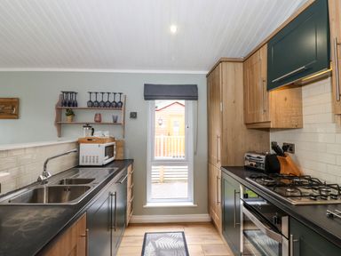 A kitchen with a sink microwave oven gas stove and wooden cabinets at Claife View Lodge in Troutbeck Bridge