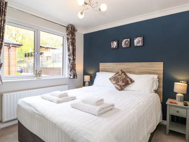 A bedroom with a double bed bedside tables and a window at Claife View Lodge in Troutbeck Bridge