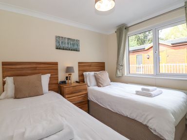 A bedroom with two single beds a wooden nightstand between them a lamp and a window showing an outside wooden structure at Claife View Lodge in Troutbeck Bridge