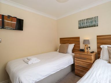 A bedroom with two single beds separated by a wooden nightstand with a lamp and clock at Claife View Lodge in Troutbeck Bridge