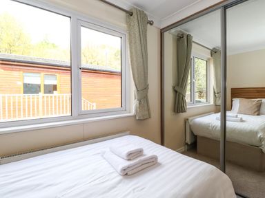 A bedroom with a bed with white linens folded towels on top and mirrored sliding door wardrobe at Claife View Lodge in Troutbeck Bridge