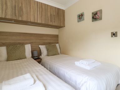 A bedroom with two single beds white linens pillows and towels with wood cabinets above at Claife View Lodge in Troutbeck Bridge
