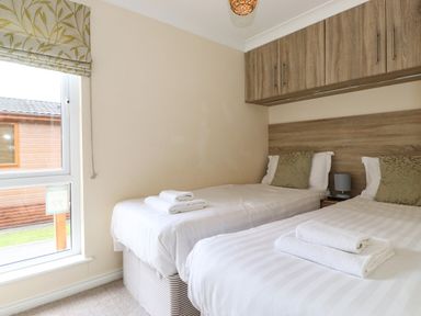 A bedroom with two single beds with white bedding and towels by a window at Claife View Lodge in Troutbeck Bridge