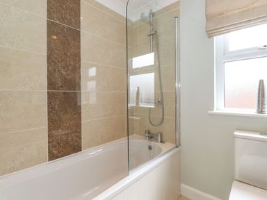 A bathroom with a bathtub and shower with tiled walls and a window next to a toilet at Claife View Lodge in Troutbeck Bridge