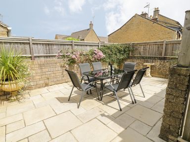 An outdoor patio with a glass table and six chairs surrounded by a stone wall and wooden fence at Rosemary Cottage in Bourton-on-the-Water