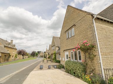 A row of stone houses along a street with flower pots on the pavement and climbing plants on the walls at Rosemary Cottage in Bourton-on-the-Water