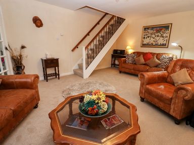 A living room with brown leather sofas a glass topped coffee table with flowers and a staircase in the background at Rosemary Cottage in Bourton-on-the-Water