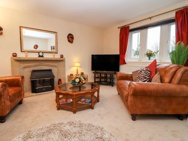 A living room with a fireplace a leather sofa and armchair a coffee table and a television at Rosemary Cottage in Bourton-on-the-Water