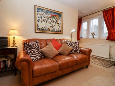 A living room with a brown leather sofa with cushions and a side table with a lamp and books at Rosemary Cottage in Bourton-on-the-Water
