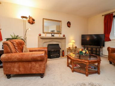 A living room with leather armchairs a coffee table with flowers a television and a fireplace at Rosemary Cottage in Bourton-on-the-Water