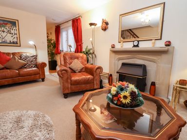 A living room with leather furniture a glass coffee table with flowers and a fireplace at Rosemary Cottage in Bourton-on-the-Water