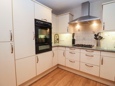 A kitchen with white cabinets a built in oven a gas stove and utensils in a holder at Rosemary Cottage in Bourton-on-the-Water