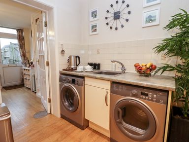 A utility room with a washing machine dryer sink kettle fruit bowl and wall clock at Rosemary Cottage in Bourton-on-the-Water