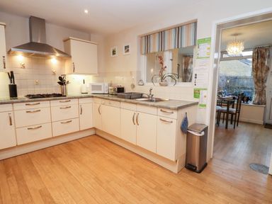 A kitchen with cream cabinets wood flooring a gas stove a microwave and a window looking into a dining area at Rosemary Cottage in Bourton-on-the-Water